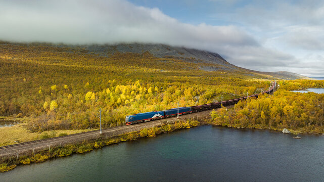 Drone view of freight train moving on track amidst greenery and lake against sky