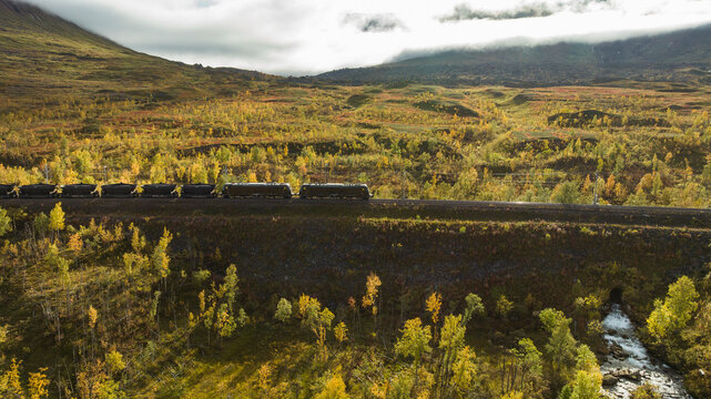 Drone shot of freight train passing through lush green landscape at sunny day