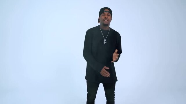 Dolly tracking shot of man performing gestures and singing in white seamless studio as camera moves from full body to chest framing