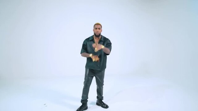Tracking shot of man gesturing and dancing while wearing gold jewelry and black outfit in white studio background