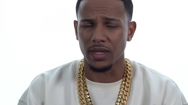 Static close up shot of man speaking and emoting in white studio headshot with gold chains, high key lighting and minimal camera movement