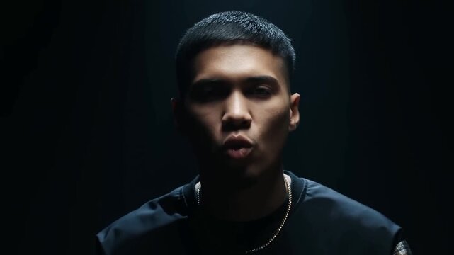 Static closeup of young man speaking with low rim lighting in dark studio backdrop, subtle movement and intimate portrait performance