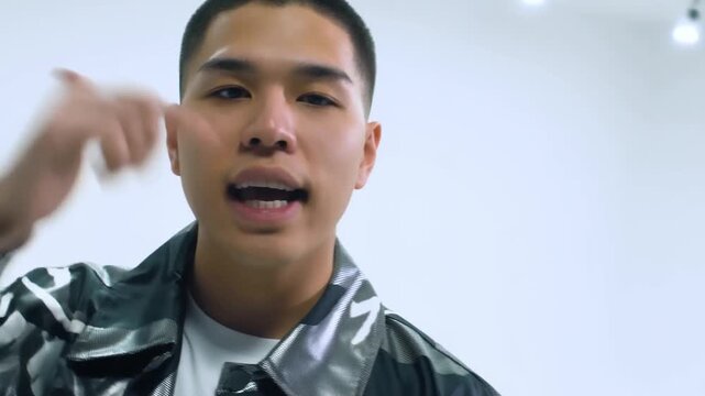 Handheld tracking shot of young man rapping and gesturing in white studio room with close up portrait movement and expressive performance