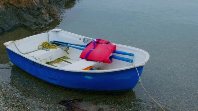 Blue Rowboat with Red Life Jacket on Coastal Shoreline
