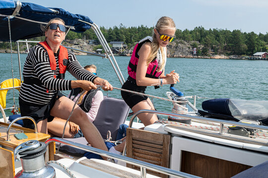 Girl helping mother with cable winch while yachting in sea during vacation trip
