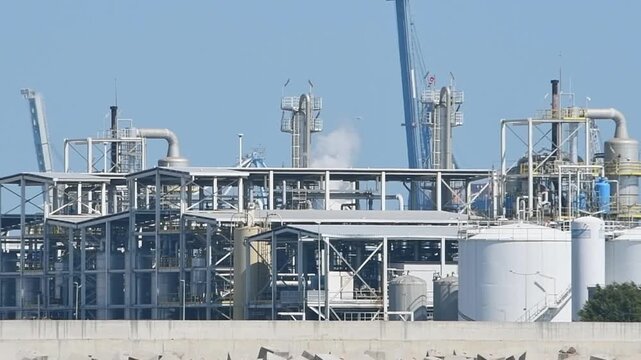 Smoky oil refinery complex, metal structures, storage tanks on a pier with breakwaters. Marine terminal for receiving, distributing oil from tankers. War Iran. Kuwait, Strait of Hormuz, Kharg Island	