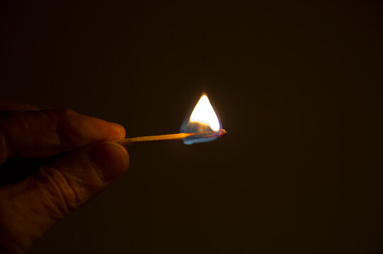Hand on unrecognizable person holding burning matchstick in dark