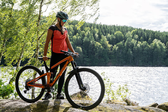 Full length of female cyclist standing with cycle near river in forest