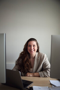 Portrait of smiling long haired female business entrepreneur sitting at office desk