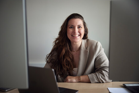 Portrait of smiling long haired female entrepreneur sitting at office desk