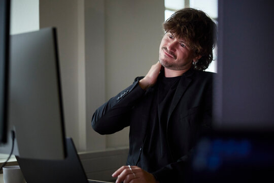 Male business professional stretching while working on desktop PC in office
