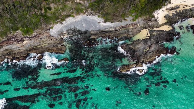 Aerial drone video downward view of waves rolling onto the rocky coastline of McBrides Beach in Forster. The top down perspective highlights ocean movement and natural coastal formations.
