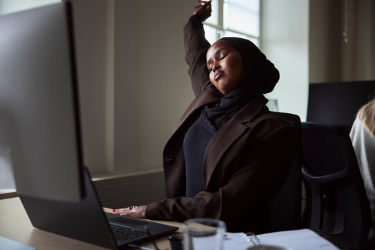 Tired female business expert stretching while sitting at office desk