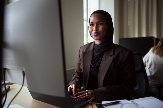 Smiling female tech expert using laptop and computer while sitting at desk in office