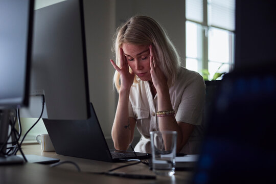 Exhausted young businesswoman touching temples while sitting at desk in office