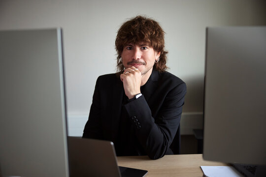 Portrait of male entrepreneur sitting with hand on chin at office desk
