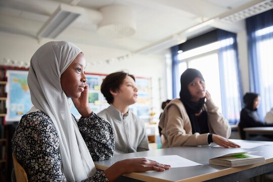 Girl in hijab sitting at desk with friends in classroom