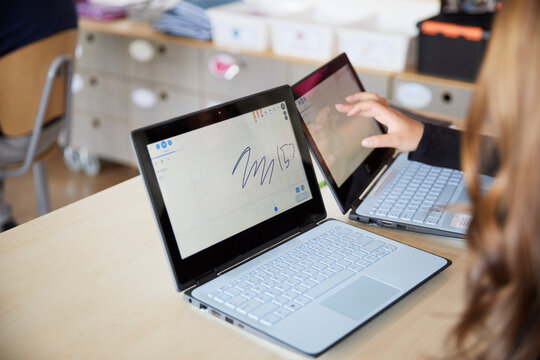 Students using touch screen laptops while sitting at desk in classroom