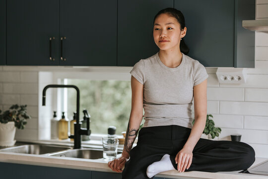 Full length of young woman sitting on kitchen counter at home
