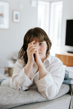 Portrait of young woman leaning on sofa in living room at home