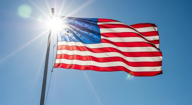 American flag waving in the wind with sun shining behind it on a clear blue sky day