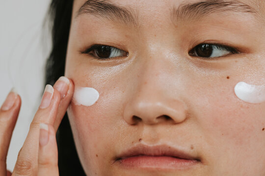 Close-up shot of young woman applying face cream