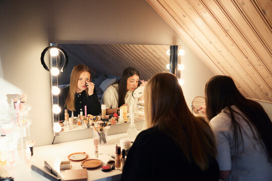 Teenage female friends getting dressed while looking in mirror at home