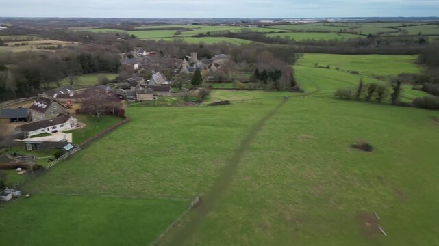 Aerial drone view of Twywell stone cottages and church with green fields Northamptonshire England