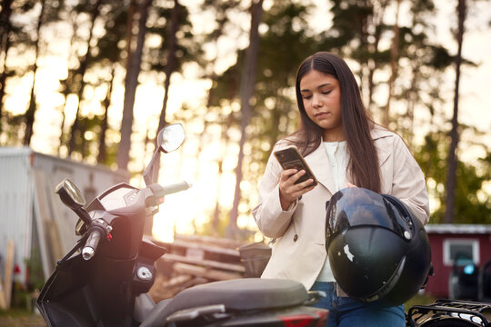 Teenage girl scrolling smart phone while standing by scooter outdoors