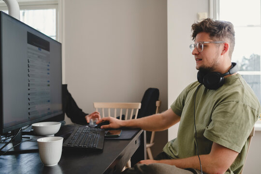Man using computer while sitting with headphones around neck at home
