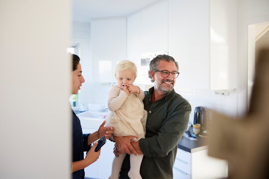 Smiling man carrying his daughter while standing in kitchen at home