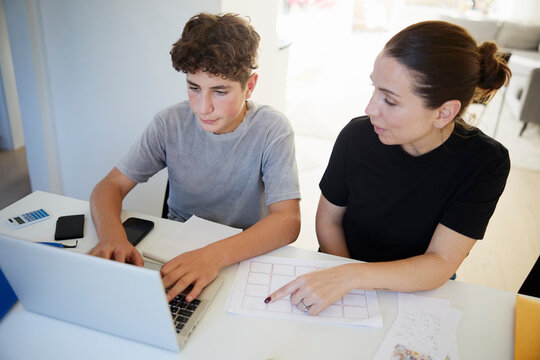 High angle view of mother assisting her son while studying at home