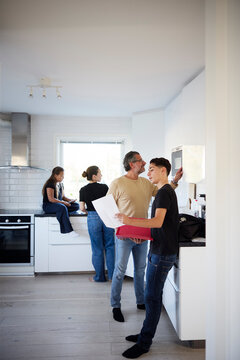 Boy showing exam papers to his father working in kitchen at home