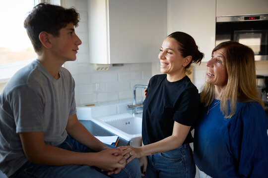 Happy woman and her sister spending leisure time with boy in kitchen at home