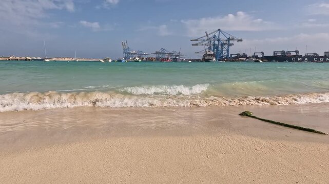 View of a marine industrial port from a sandy urban beach in Birzebbuga, Malta