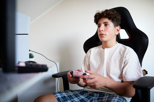 Focused boy playing video game while sitting on chair at home