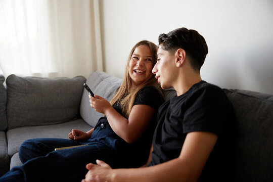 Brother and sister spending leisure time while sitting on sofa at home