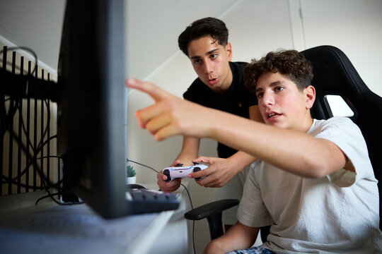 Boy pointing at screen while brother playing video games with joystick at home