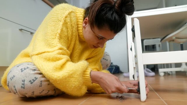 Woman Searches Floor. Young Woman On Tiled Floor Carefully Seeking Tiny Missing Item Near Furniture Leg
