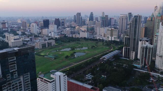 Unique tripod aerial view of Royal Bangkok Sports Club and city skyline featuring modern skyscrapers and skytrain station at dusk. Bangkok, Thailand May 2. 2025