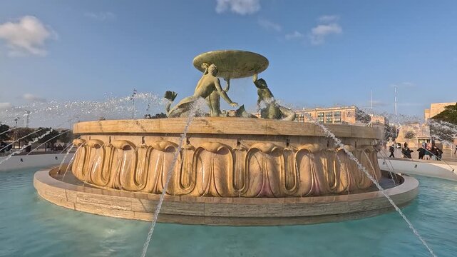 The cascading jets of the Triton Fountain in Valletta glow in the golden evening sunlight, slow motion
