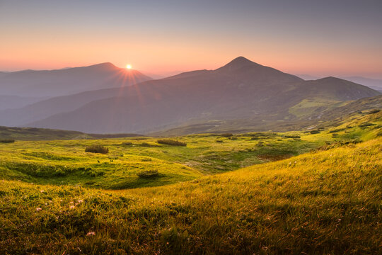 Incredible sunset with golden sunlight casting a warm glow over lush grassy meadows in the summer mountains. Landscape photography