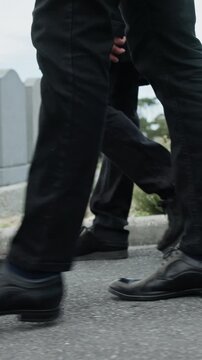 Feet, people and walking at cemetery for funeral procession, mourning and loss at ceremony. Legs, shoes and group for steps on ground, outdoor or grief at graveyard with farewell, support and death