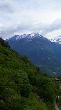 Majestic alpine landscape featuring lush green mountainsides in the foreground leading up to rugged snow-capped peaks under a dramatic, cloudy sky. This pristine natural environment showcases the b...