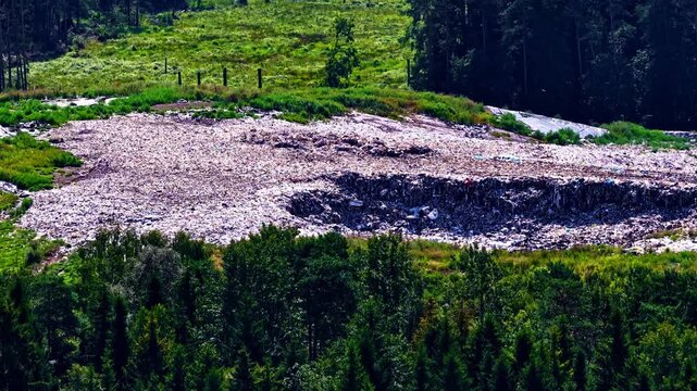 A landfill clearing cuts through forest, showing exposed waste and greenery. Rural setting contrast - aerial drone view
