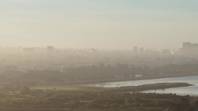 Aerial footage showing a hazy morning sunrise over the city of Berkeley, California, with views of Cesar Chavez Park and the city skyline shrouded in warm, golden light and atmospheric fog