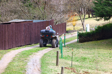 Person riding an ATV along a narrow rural path, capturing the atmosphere of spring farm work, countryside movement, practical outdoor tasks and the everyday rhythm of life in a gardening and orchard © Gabriela