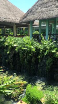 Lush Tropical Garden with Small Waterfall and Thatched Roof Buildings