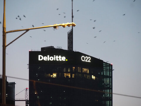Illuminated Deloitte and Q22 signs on a modern skyscraper facade at night in Warsaw