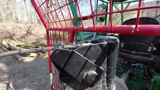 Close-up of a heavy-duty steel cable winch operating on a forestry tractor